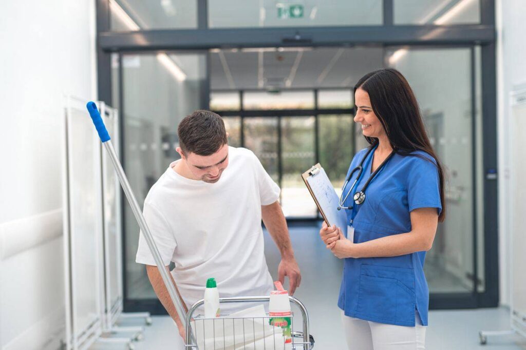 Young man with down syndrome working in a hospital as cleaner, talking to nurse, having fun. Concpet of integration people with disability into society.